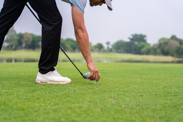 Close up of a golfer's hand placing golf ball on tee over green grass.