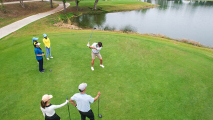 Drone view of young pro golfers swings the club on scenic golf course.
