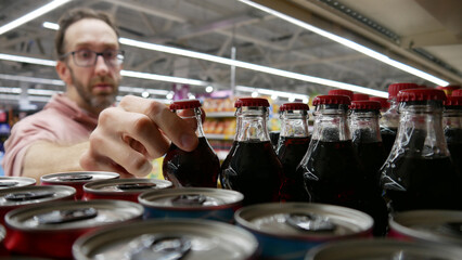 A male customer taking a glass bottle of cola in a grocery store