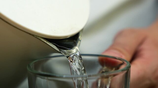 Electric kettle with hot water.
Boiled water from the kettle pours into a glass cup in the kitchen.
White electric kettle fills an empty cup with water