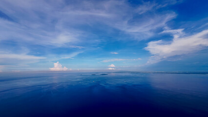 Fototapeta premium Aerial view of a flat calm sea surface and white clouds. Small clouds above the ocean surface. View from above of a calm ocean surface, small tropical islands and ships moving on the sea.