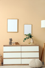 Chest of drawers with branches in vase, books and frames on beige wall in room