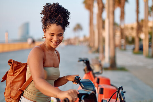 Happy young woman renting an electric scooter on Barceloneta beach in Barcelona, sustainable mobility concept