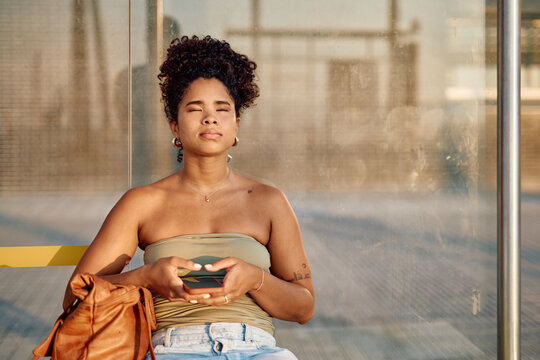 Serene young woman meditating while waiting for public transportation, finding peace in the urban environment