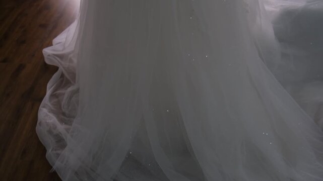 A stunning, voluminous white wedding gown is elegantly displayed on a mannequin. The strapless bodice features delicate pearl embellishments and a satin sash cinching the waist. 