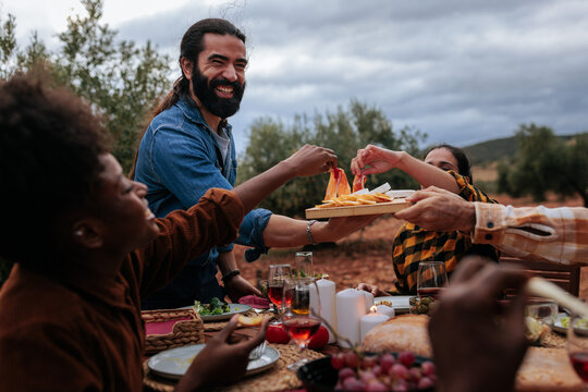 Friends sharing appetizers at outdoor dinner party in olive grove
