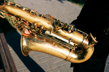 Obraz premium Close-up of vintage brass saxophone in musicians hands outdoors in sunlight
