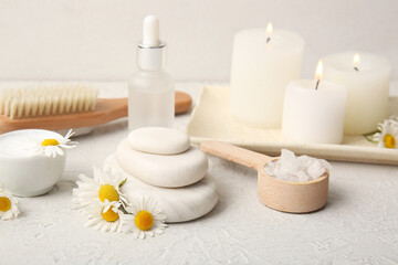 Chamomile flowers, scoop with sea salt and bottle of cosmetic product on grey grunge background, closeup