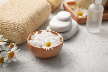 Wooden bowl with sea salt and chamomile flower on grey grunge background, closeup