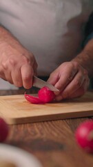 Close-up view of hands meticulously slicing a vibrant red radish on a light wooden cutting board.