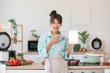 Young woman with blank tablet computer cooking in kitchen