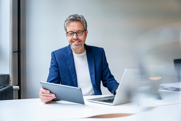 Confident businessman working with tablet and laptop at office desk