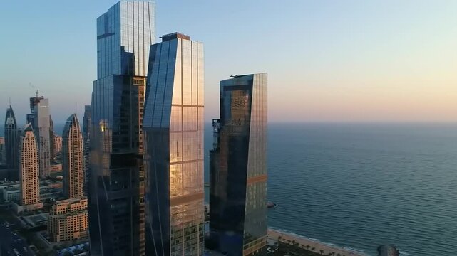 Aerial view of modern skyscrapers along the coastline at sunset with ocean waves gently lapping