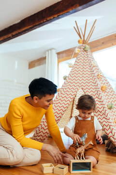 Smiling woman sitting by son playing with toy animals at home