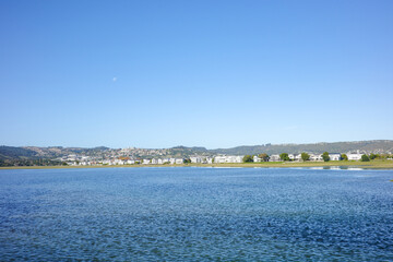 A calm lagoon with gentle rippling water reflecting the bright blue sky, with a charming coastal town and hills as backdrop. The peaceful view with scenic view of travel and lifestyle