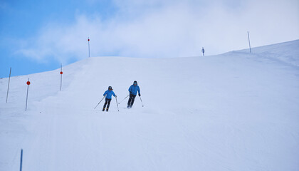 Two skiers descending wide snowy slope at mountain resort on winter day