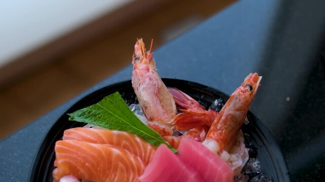 Assorted sashimi and sushi, including salmon, tuna, scallop, and salmon roe, presented on a plate with garnishes, smoothly rotating under studio lighting. High quality 4k footage