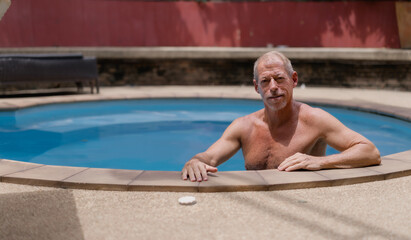 Relaxed senior man enjoying summer vacation while lounging in a private home swimming pool,...