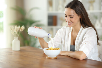 Happy woman pouring milk on cereals for breakfast at home