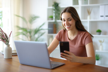Fototapeta premium Happy woman using phone and computer on a table at home