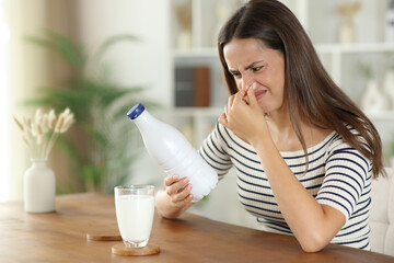 Woman covering nose smelling expired milk looking expiry date on bottle