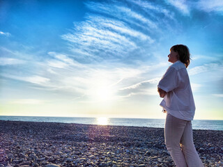 Mature blonde woman enjoying a serene moment by the beach during sunset while documenting her travel adventures