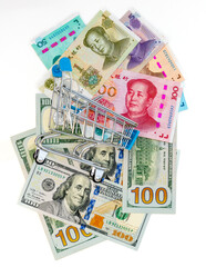 Mini Shopping Cart on Scattered US Dollar and Chinese Yuan Banknotes. International Finance and Trade Concept.