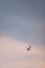 A commercial airplane soaring through a pastel sky at sunset, with soft clouds and a warm, tranquil atmosphere.