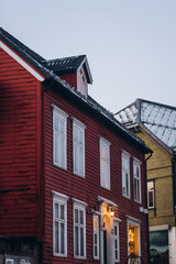 A charming red wooden house in Tromsø, Norway, features a glowing star decoration in the window, with a snow-covered rooftop and warm lights, capturing a festive, cozy winter atmosphere.