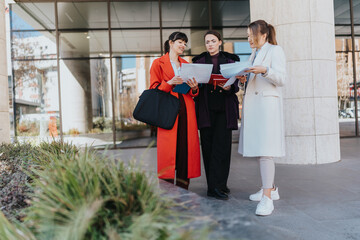 Three business professionals collaborate outdoors while analyzing documents in a vibrant urban setting. The team represents a dynamic work environment, teamwork, and the modern workplace.