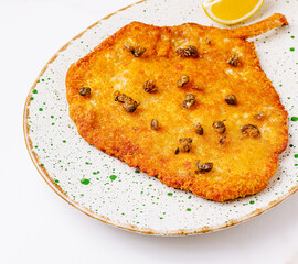 Delicious crispy schnitzel fish dish served with lemon on a textured plate