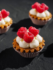 Delicious raspberry tarts with cream served on a dark slate surface