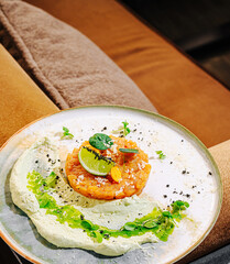 Gourmet salmon tartare served with creamy avocado mousse, lime, fresh herbs, and artistic plating, fine dining seafood appetizer in a modern restaurant setting.