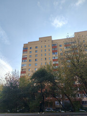 A high-rise residential building featuring a mix of red and beige brick, with small balconies and air conditioning units. The image captures the practical and functional design of city apartment