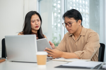 Businesswoman or office worker looking intently at tablet holding in a man's hand at working table.