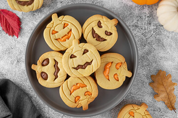 Halloween pumpkin shaped sandwich cookies with sweet cream filling on a gray plate with milk on a concrete background. Jack o lantern cookies. Top view.