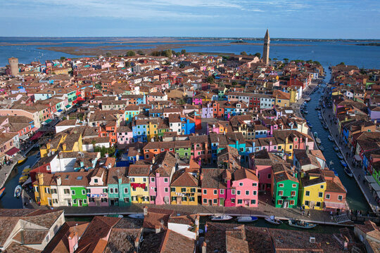 Aerial view of a rainbow of vibrant homes cascade across the island, punctuated by the iconic leaning tower of Burano, Venice, Veneto, Italy.