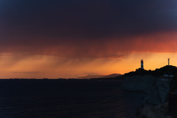 Dramatic sunset over the sea with lighthouse silhouette and glowing sky.