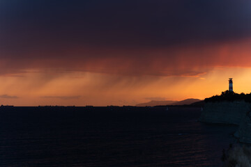Naklejka premium Dramatic sunset over the sea with lighthouse silhouette and glowing sky.