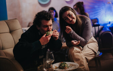 Two friends seated comfortably at a lounge enjoy their meal in a relaxed setting. The ambiance features warm lighting and a casual atmosphere, creating an inviting and friendly dining environment.