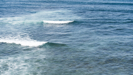 Blue ocean waves with white foam rolling on the surface of clear water.