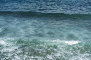 Fototapeta premium Blue ocean waves with white foam rolling on the surface of clear water.