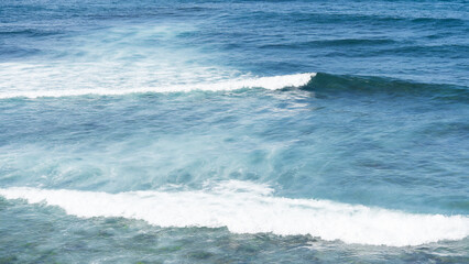 Fototapeta premium Blue ocean waves with white foam rolling on the surface of clear water.