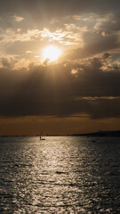 Scenic sunset over the sea with sailboat silhouette and dramatic sky.