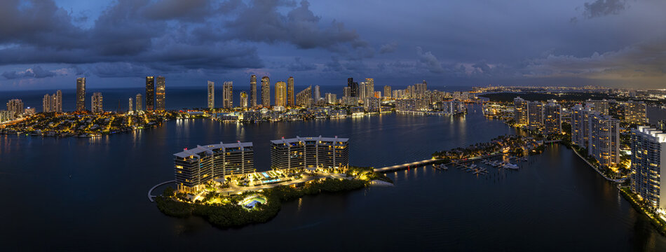 Aerial view of the illuminated waterfront buildings casting shimmering reflections onto the dark waters of Dumfoundling Bay, Aventura, Florida, United States.