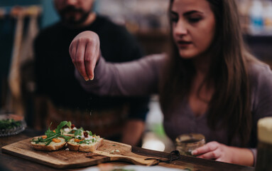 Fototapeta premium A young woman adds garnish to slices of bread in a relaxed bar environment. The scene is casual yet focused on food preparation and culinary creativity.