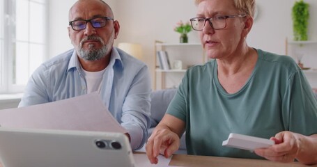 Elderly couple at home manage finance, comparing paperwork and figures on a tablet planning a budget and a discussion of options together. Seniors review bills calculating taxes in retirement - Powered by Adobe
