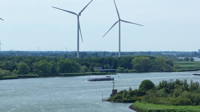 Wind turbines spin by river with passing cargo ship, tranquil scene in Barendrecht