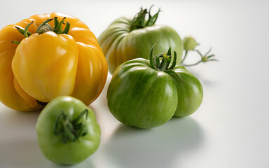 Fresh yellow and green tomatoes arranged on a white surface showcasing their vibrant colors and unique shapes