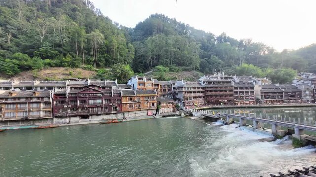 Time lapse of wooden boats moving along the Tuojiang River in Fenghuang Old Town, Hunan, with stilt houses and traditional Chinese architecture by the water.